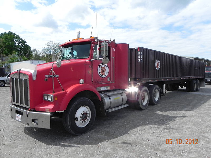 Truck with a container trailer staged on the paved storage yard